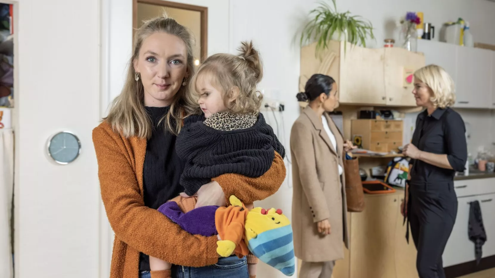 Lisette de Beer houdt kind vast op haar werk. Op de achtergrond de moeder van het kind en HR-adviseur Marije Tolsma