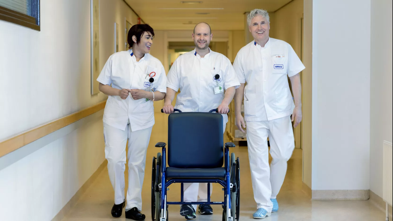 Gerard met zijn teamgenoten Jasmin (links) en Geert (rechts) achter een rolstoel in een gang van het ziekenhuis UMCG