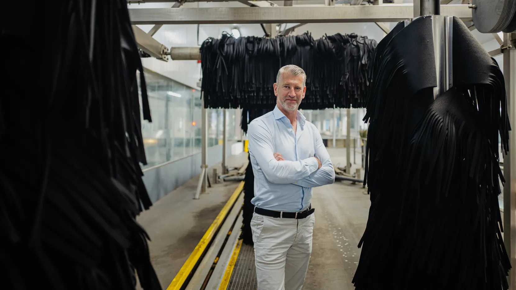 Martin Kniest staat in een wasstraat tussen de grote zwarte wasdraaiers. Zijn armen houdt hij gekruisd voor zn borst.