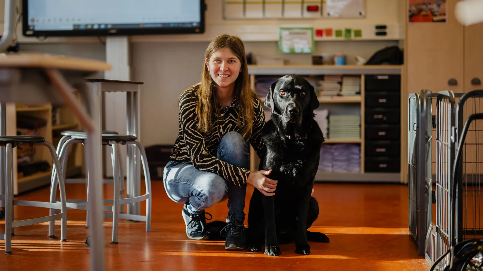 Portret van Kim. Ze is in de klas en zit gebukt naast haar hulphond.