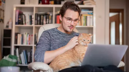 Jonge man zit op een stoel en is bezig met werk vinden terwijl een kat op schoot zit