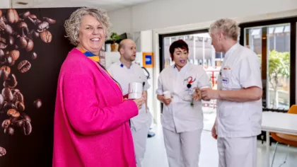 Portret van Gré met op de achtergrond Gerard die met hulp van een jobcoach werkt. Hij staat links van zijn collega's Yasmin en Geert.