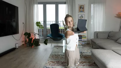 Een foto van Eva staand in haar woonkamer met haar laptop vast