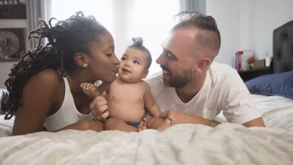 Gezin in thuissituatie: moeder en vader liggen op bed met een baby ertussen