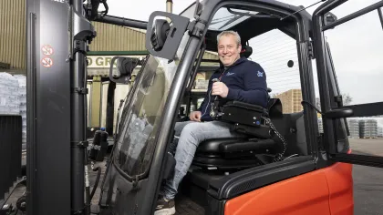 Portret van Ronald. Hij zit in zijn aangepaste heftruck en kijkt lachend naar de camera.
