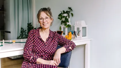 Portret van Conny. Ze heeft een rood roze jurk aan en zit op een stoel. Ze kijkt glimlachend naar de camera. 