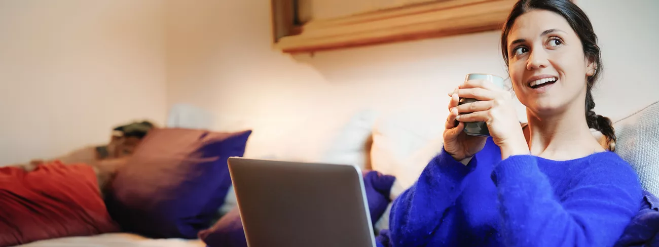 Vrouw die een kop thee drinkt op de bank met haar laptop op schoot