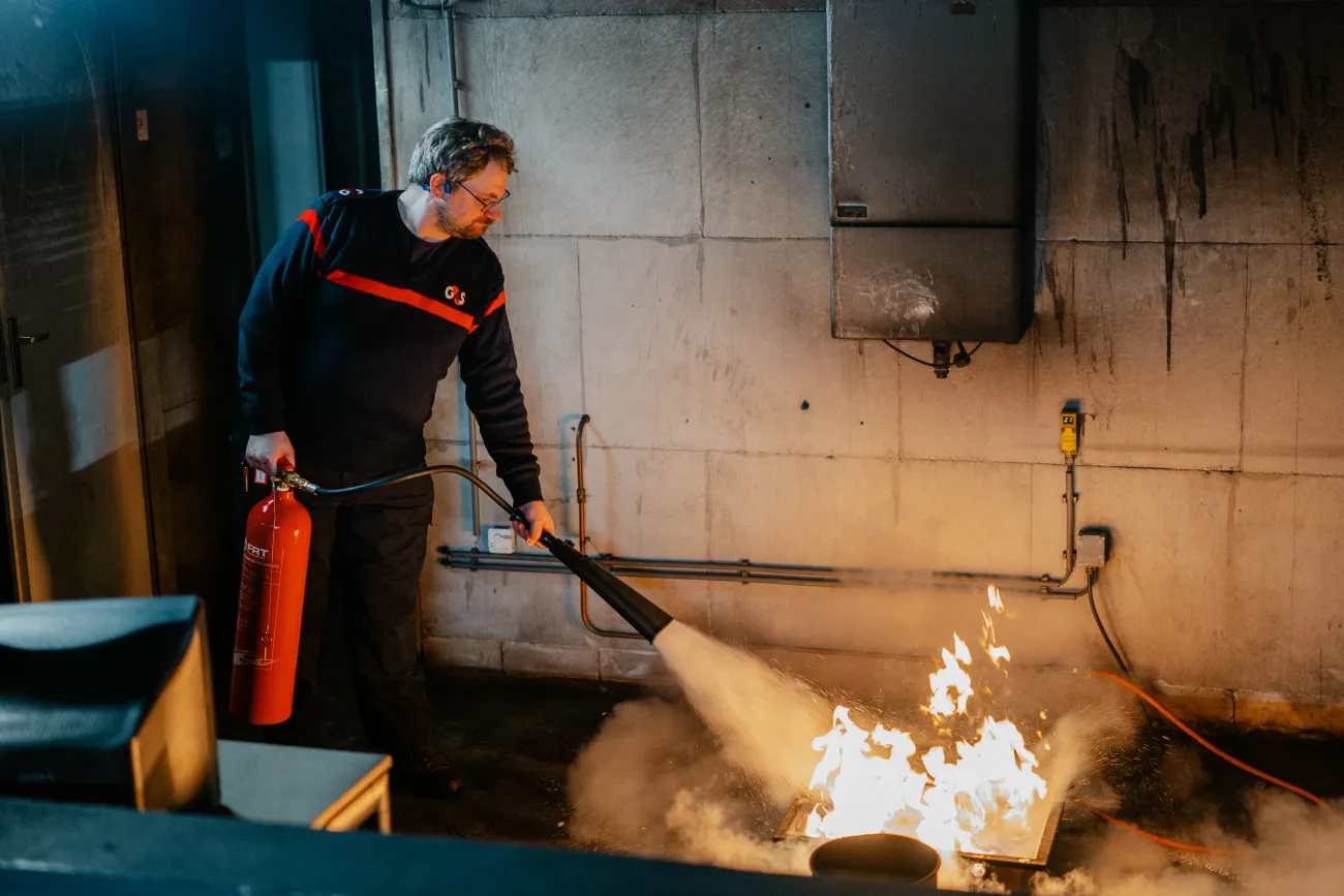 Fransz is aan het werk en brandblusapparatuur aan het testen. Hij blust een brandje.