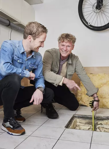 Portret van energiecoach Martijn en klant Kasper. Ze zitten beiden gehurkt bij een luik naar de kruipruimte.