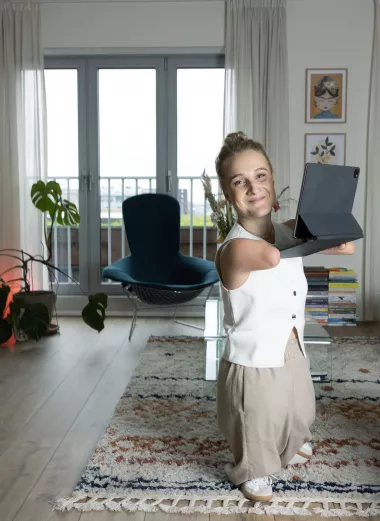 Een foto van Eva staand in haar woonkamer met haar laptop vast