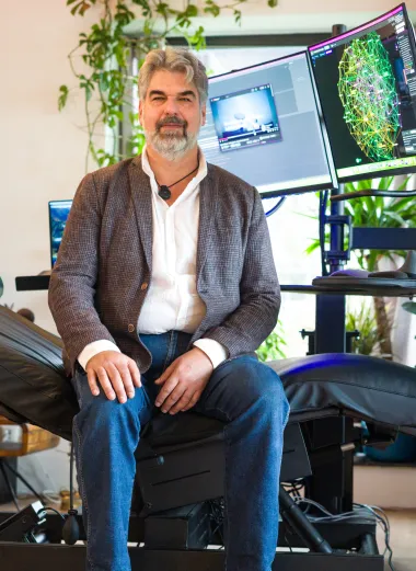 Portret van Bjorn. Hij zit op zijn speciale in hoogte verstelbare ligstoel. Aan de voorkant van de ligstoel zijn er 2 computerschermen verbonden om te kunnen werken. 