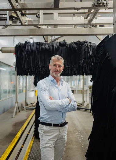 Martin Kniest staat in een wasstraat tussen de grote zwarte wasdraaiers. Zijn armen houdt hij gekruisd voor zn borst.