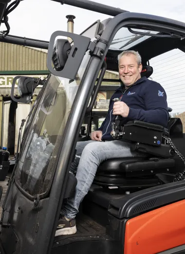 Werknemer Ronald zit in zijn aangepaste heftruck, hij steekt zijn duim op.