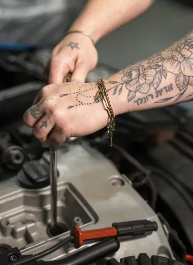 Portret van Jacintha. Ze is aan het werk aan een auto. Je ziet alleen haar armen. Op haar armen staan meerdere tattoos. 