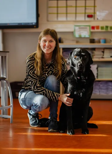 Portret van Kim. Ze is in de klas en zit gebukt naast haar hulphond.