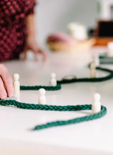 Conny is bezig met een handeling uit de cursus 'Sterk met pijn’. Ze verplaatst op tafel witte figuren rondom een groen koord. 