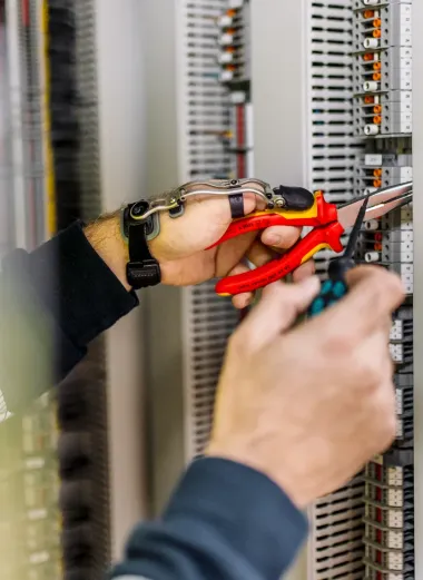 Portret van Siemen zijn duimprothese. Hij is aan het werk en houdt met zijn handen, waarvan de linkerhand de duimprothese bevat, gereedschap vast. Hij staat voor een kast. 